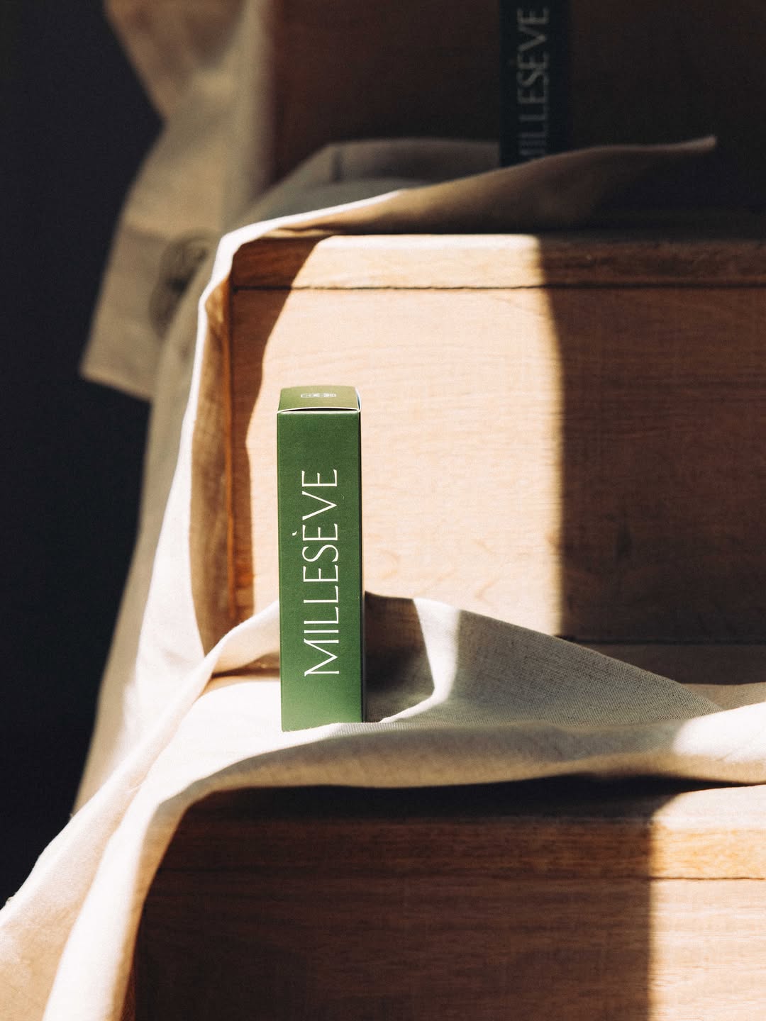 Un étui de parfum Millesève posé sur un tissu en lin et un escalier en bois.